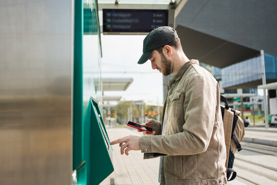 Young man using ticket machine at public transport station in city