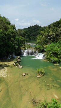 Aerial view of Pangas Falls cascading into a turquoise pool surrounded by lush tropical jungle and palm trees in Bilar, Central Visayas, Philippines.