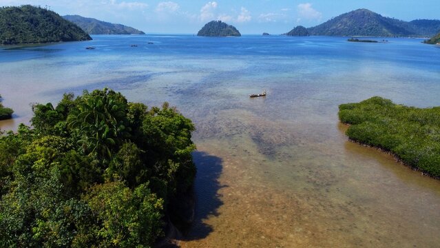 Aerial view of Mandeh islands with lush green vegetation, clear turquoise waters, and a small traditional boat in Koto XI Tarusan, West Sumatra, Indonesia.