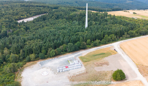 Aerial view of construction site for a wind turbine farm with concrete tower segments and foundation area near a forest and existing turbine, Trier-Saarburg, Rhineland-Palatinate, Germany.