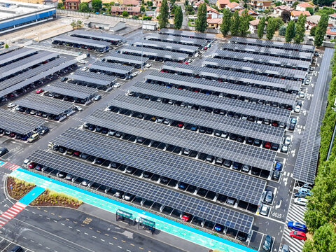 Aerial view of a large solar car park with rows of photovoltaic panels providing shade for parked cars in Rivalta di Torino, Piedmont, Italy.
