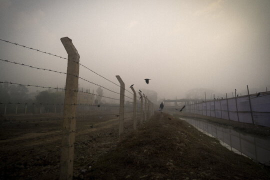 Sherpur, Sylhet Division, Bangladesh - 01 January 2026: View of a barbed-wire fence along a canal in the misty morning light with a person walking in the distance.