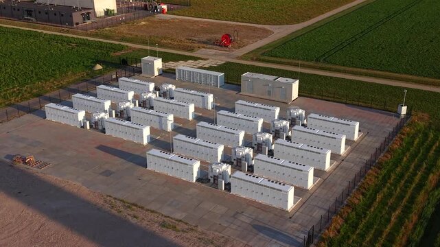 Aerial view of a battery energy storage system with white containers on a concrete pad surrounded by agricultural fields in Dronten, Flevoland, Netherlands.