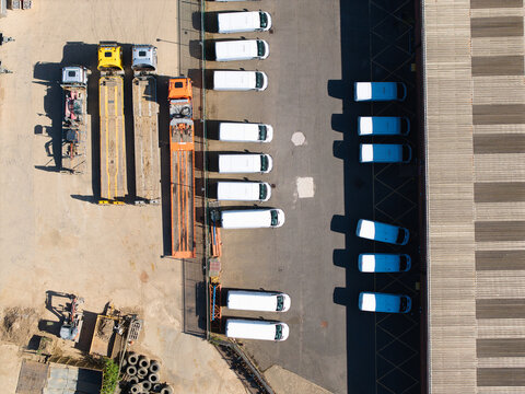 Aerial view of a logistics yard featuring rows of parked white vans and heavy-duty trucks on an asphalt surface in Lutterworth, England, United Kingdom.