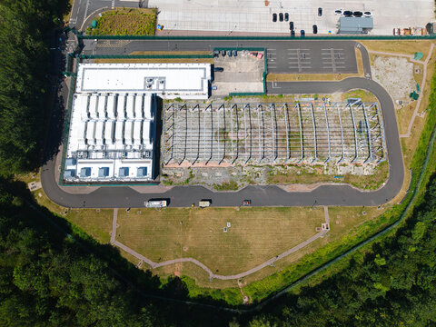 Aerial view of the ATOS data center facility with a modern building, cooling units, and an adjacent steel frame structure in Birmingham, England, United Kingdom.