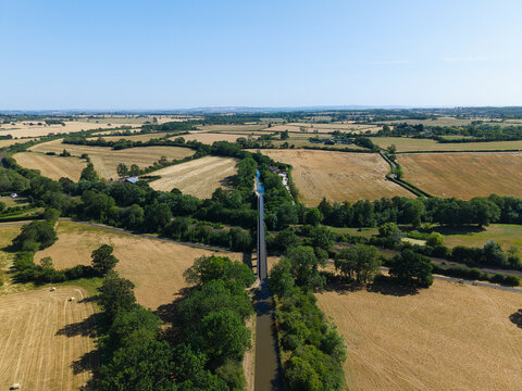 Aerial view of Edstone Aqueduct, a historic narrow boat bridge spanning over fields and trees in the English countryside, surrounded by golden farmland in Wootton Wawen, England, United Kingdom.