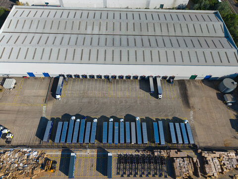 Aerial view of the Daventry International Rail Freight Terminal with a large warehouse, loading bays, and rows of parked semi-trailers in the yard in Kilsby, England, United Kingdom.