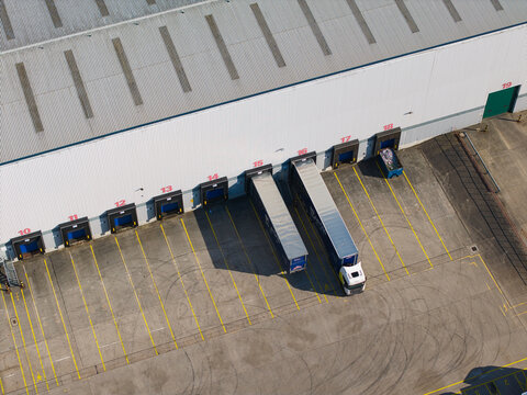 Aerial view of the Daventry International Rail Freight Terminal featuring warehouse loading bays, numbered doors, a parked truck, and yellow markings in Kilsby, England, United Kingdom.