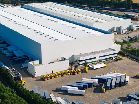 Aerial view of Daventry International Rail Freight Terminal with large warehouses, rows of yellow HGVs, and parked trailers in a logistics center in Kilsby, England, United Kingdom.