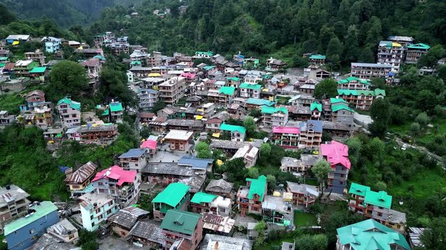 Aerial view of Manali town with colorful rooftops nestled in the lush green Himalayan mountains in Manali, Himachal Pradesh, India.