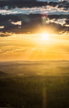 Aerial view of the sunset over the Laaminki forest landscape with dense trees and rolling hills under a dramatic golden sky in Kangasniemi, Etela-Savo, Finland.