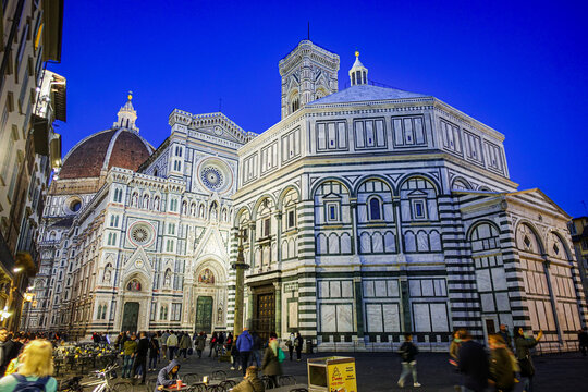 Florence, Italy - 22 April 2017: View of the Florence Cathedral and the Baptistery of Saint John at dusk, with tourists walking in the square.