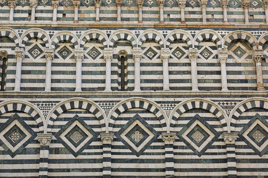 View of the intricate green and white striped marble facade of the Pistoia Cathedral with its rhythmic arches and geometric patterns in Province of Pistoia, Tuscany, Italy.