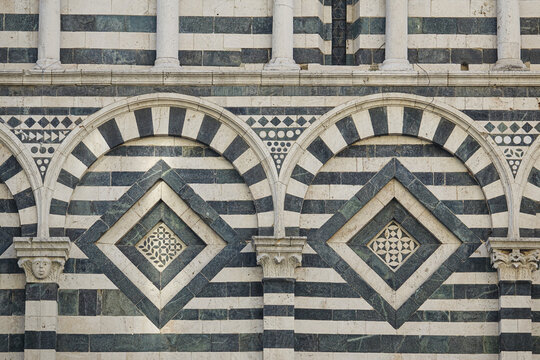 View of the intricate black and white marble facade of the Pistoia Cathedral with Romanesque arches and geometric stone inlays in Province of Pistoia, Tuscany, Italy.