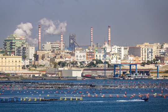 View of the industrial skyline of Taranto with steelworks smokestacks rising above the city buildings and mussel farms in the foreground waters in Taranto, Apulia, Italy.