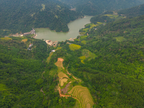 Aerial view of a reservoir surrounded by lush green mountains and terraced rice fields with a dam structure visible in the distance in Tien Du, Bac Ninh, Vietnam.