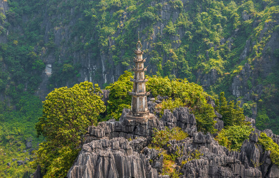 Aerial view of the stone pagoda atop the Mua Cave viewpoint, surrounded by dramatic limestone karst mountains and lush green vegetation in Nam Hoa Lu, Ninh Binh, Vietnam.