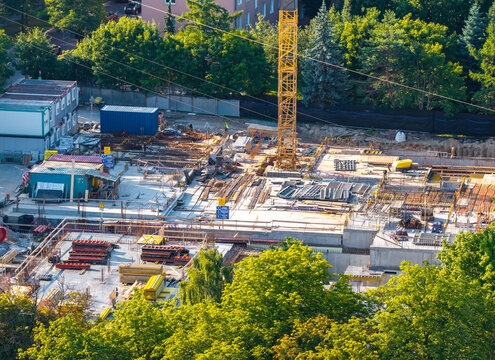 Aerial view of a construction site with a yellow crane, steel rebar, concrete foundations, and shipping containers surrounded by trees in Sopot, Pomeranian Voivodeship, Poland.