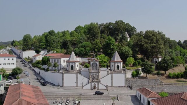 Aerial view of the Santuario de Nossa Senhora de Porto de Ave with its distinctive twin towers, stone staircases, and surrounding lush green trees in Taide, Braga, Portugal.