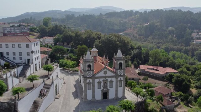 Aerial view of Santuario de Nossa Senhora de Porto de Ave with its twin bell towers and terracotta roof set amidst the lush green hills of Taide, Braga, Portugal.