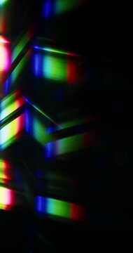 Light rays shining into a glass prism causing an optical effect of a dazzling rainbow of sparkling lights. Reflective streaks of angled lighting creating a visual of brilliant shining colors. Loop.