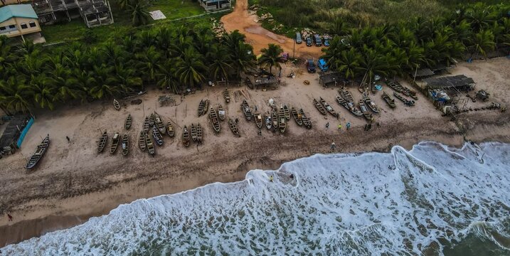 Aerial view of numerous wooden fishing boats lined up on a sandy beach in Ghana.