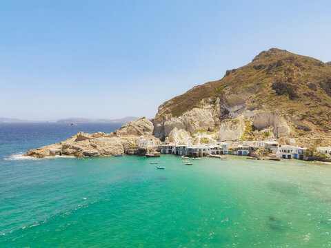 Aerial view of the colorful traditional boathouses known as syrmata nestled along the rocky coastline and turquoise waters of Klima in Milos, Greece.