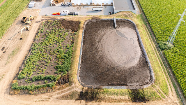 Aerial view of a large agricultural slurry lagoon next to a field with vegetation and construction machinery in a rural area of Serbia.