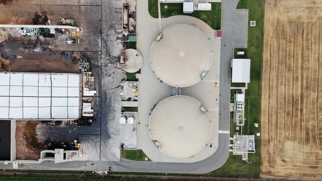 Aerial view of an industrial facility featuring two large circular storage tanks, paved access roads, and adjacent agricultural land in Serbia.