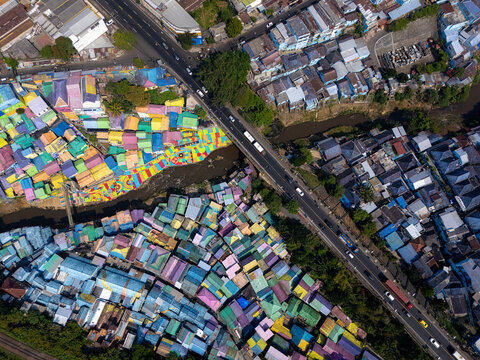 Aerial view of the colorful Jodipan village with vibrant rooftops, a river, and a bridge with traffic in Blimbing, East Java, Indonesia.