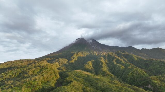 Aerial view of Mount Merapi featuring lush green volcanic slopes and clouds gathering around the summit in Kecamatan Cangkringan, Daerah Istimewa Yogya, Indonesia.