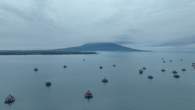 Aerial view of Grand Elty Krakatoa with numerous traditional fishing boats floating on the calm sea under a cloudy sky in Kecamatan Kalianda, Lampung, Indonesia.