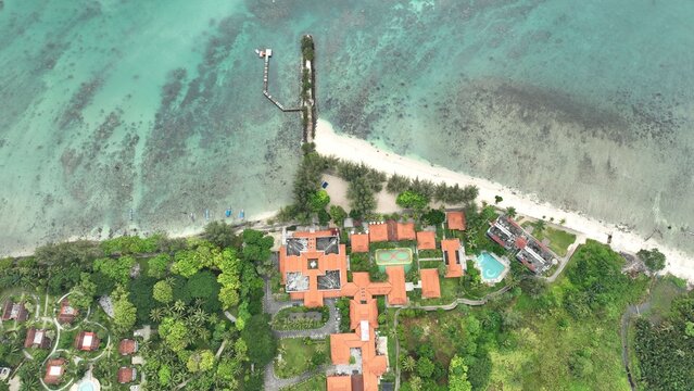 Aerial view of Grand Elty Krakatoa resort with terracotta-roofed buildings, lush gardens, swimming pool, and wooden pier extending into turquoise waters, Kecamatan Kalianda, Lampung, Indonesia.