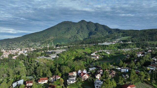 Aerial view of the lush mountainous landscape of Lembang, featuring dense green forests, residential houses, and agricultural fields in Lembang, West Java, Indonesia.