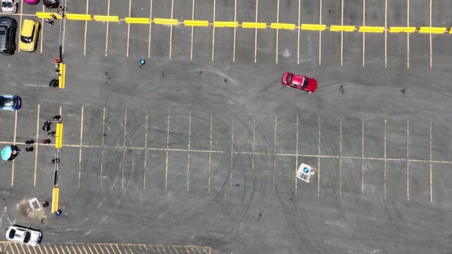 Aerial view of the parking lot at Coliseo Municipal Maestro Tomas Dones Hernandez with parked cars, people, and tire marks on the asphalt in Fajardo, Fajardo, Puerto Rico.