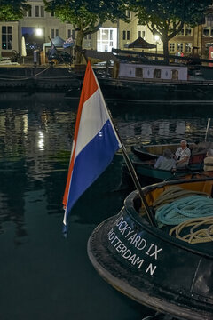 Dordrecht, Netherlands - 30 May 2026: View of the Dordt in Stoom maritime event at night, featuring a Dutch flag on a historic steam tug boat moored at the quay with people in a small vessel.