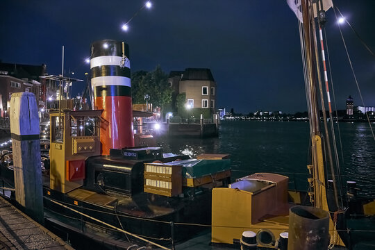 Dordrecht, Netherlands - 30 May 2026: View of a historic steam tug boat docked at the quay during the Dordt in Stoom event at night, with illuminated masts and reflections on the water.