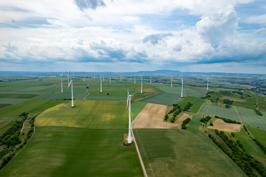 Aerial view of a wind farm with multiple white wind turbines standing in green agricultural fields under a cloudy sky in Worms, Rhineland-Palatinate, Germany.