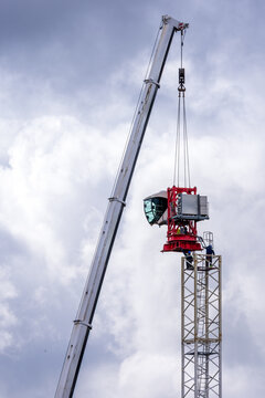 View of a mobile crane lifting the cabin section of a tower crane with workers standing on the structure under a cloudy sky in Vilnius, Vilnius County, Lithuania.