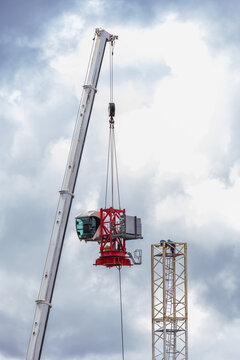 View of a mobile crane lifting a tower crane section with workers standing on the structure against a cloudy sky in Vilnius, Vilnius County, Lithuania.