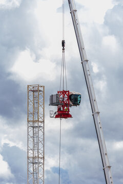 View of a mobile crane lifting a red tower crane cabin section against a cloudy sky in Vilnius, Vilnius County, Lithuania.