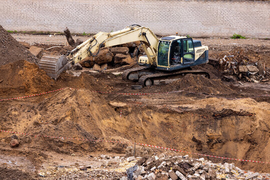 View of an excavator working at a construction site with piles of earth, debris, and a brick wall in the background in Vilnius, Vilnius County, Lithuania.