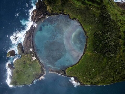 Aerial view of the volcanic islet of Ilheu de Vila Franca do Campo featuring a circular lagoon, surrounded by the Atlantic Ocean, lush green cliffs, and rocky coastline in Azores, Portugal.