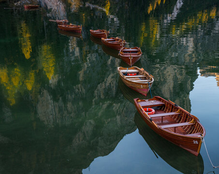 View of wooden rowboats floating on the calm, reflective water of Lago di Braies with surrounding mountain cliffs in Italy.