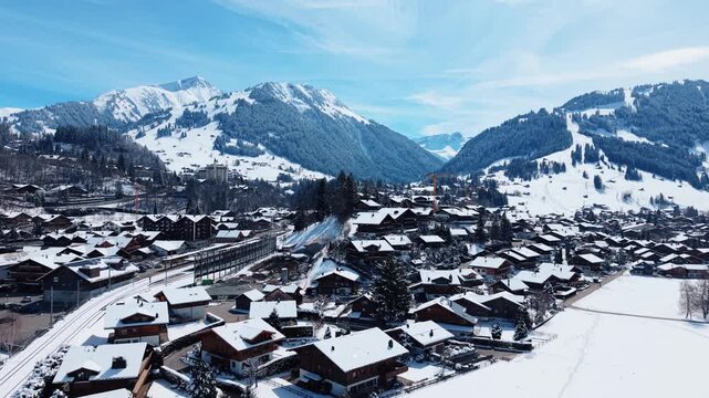 Aerial view of Gstaad village nestled in the snowy Swiss Alps with traditional wooden chalets, pine trees, and snow-covered slopes in Saanen, Canton of Bern, Switzerland.