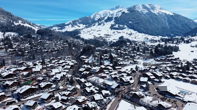 Aerial view of Gstaad village with snow-covered wooden chalets nestled in the valley surrounded by the Swiss Alps in Saanen, Canton of Bern, Switzerland.