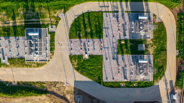 Aerial view of an electrical substation featuring high-voltage transformers, gravel pads, and surrounding green grass in Poland.