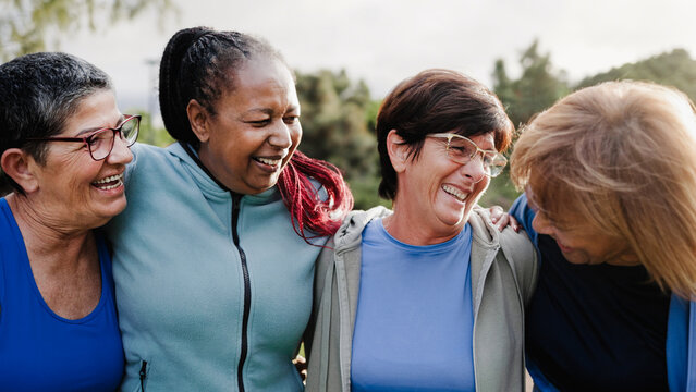 Happy multiracial senior women having fun at public park - Elderly people hugging each other