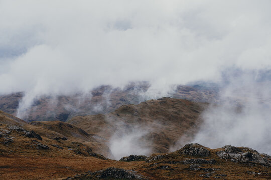 View of Y Lliwedd mountain ridge partially obscured by low-hanging clouds and mist over the rocky terrain of Snowdonia in Caernarfon, Wales, United Kingdom.