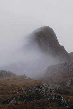 View of the rocky peak of Y Lliwedd shrouded in thick mist and low clouds above the rugged landscape in Caernarfon, Wales, United Kingdom.